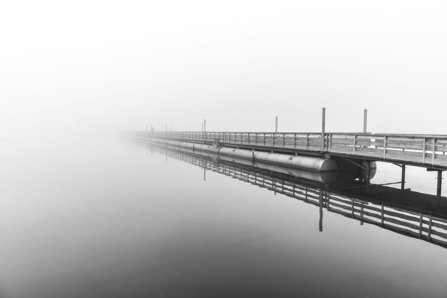 un ponte di legno e metallo in bianco e nero che si specchia sull'acqua un ponte di legno e metallo in bianco e nero che si specchia sull'acqua