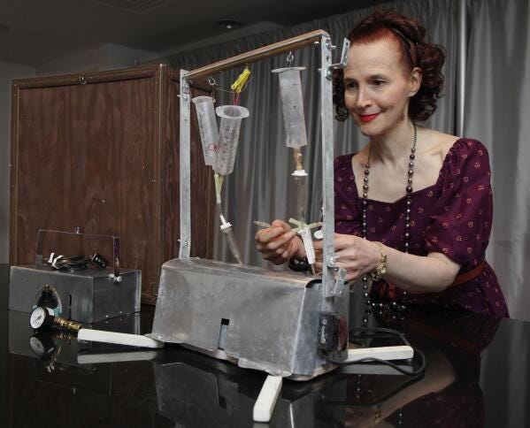 Ava Janus of Troy, Mich., the sole surviving heir of Dr. Jack Kevorkian, poses with his "Thanatron" machine, and its carry box, left, in New York Thursday Oct. 27, 2011. It is scheduled to be auctioned as part of his estate, Friday Oct. 28, 2011. Kevorkian's estate is going ahead with plans to auction 17 of his paintings, including one he did with a pint of his blood, even though a suburban Boston museum is refusing to give them up. (AP Photo/Richard Drew)