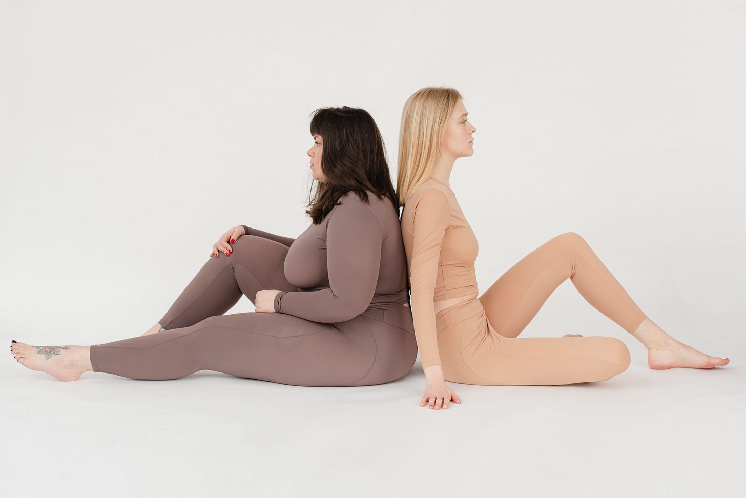 Image of two women sat back to back on the floor, one thin and one fat