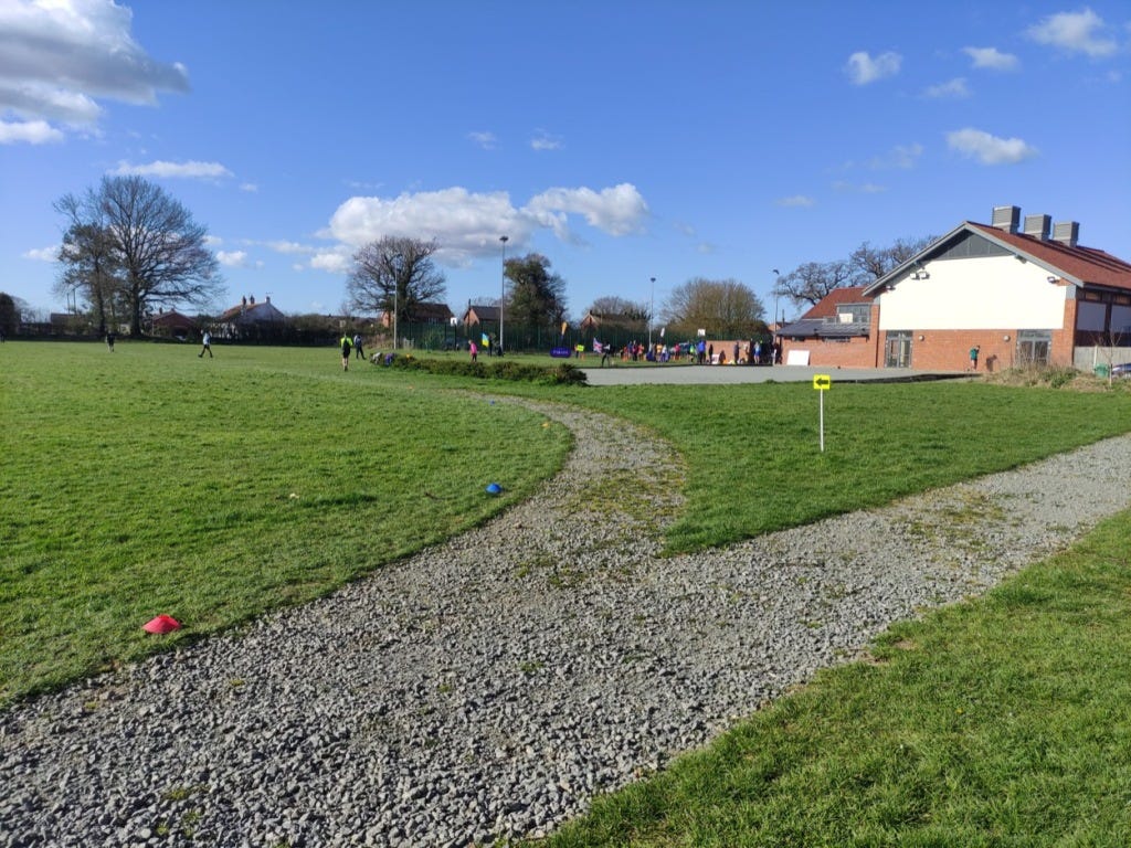 A gravelly path on the field with cones and an arrow to mark the route
