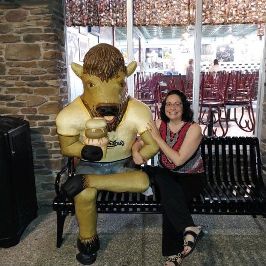 Author with statue of a buffalo eating an ice cream cone outside of an ice cream shop