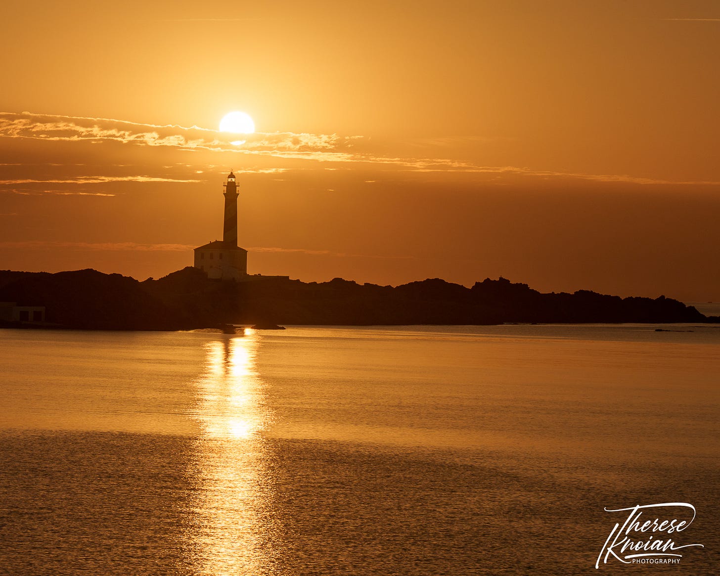 Menorca lighthouse at sunrise with reflection in the water.