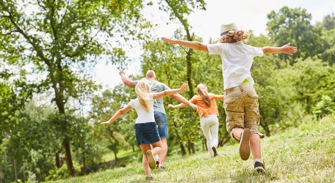 A group of four people playing outside on the grass with trees around them A group of four people playing outside on the grass with trees around them
