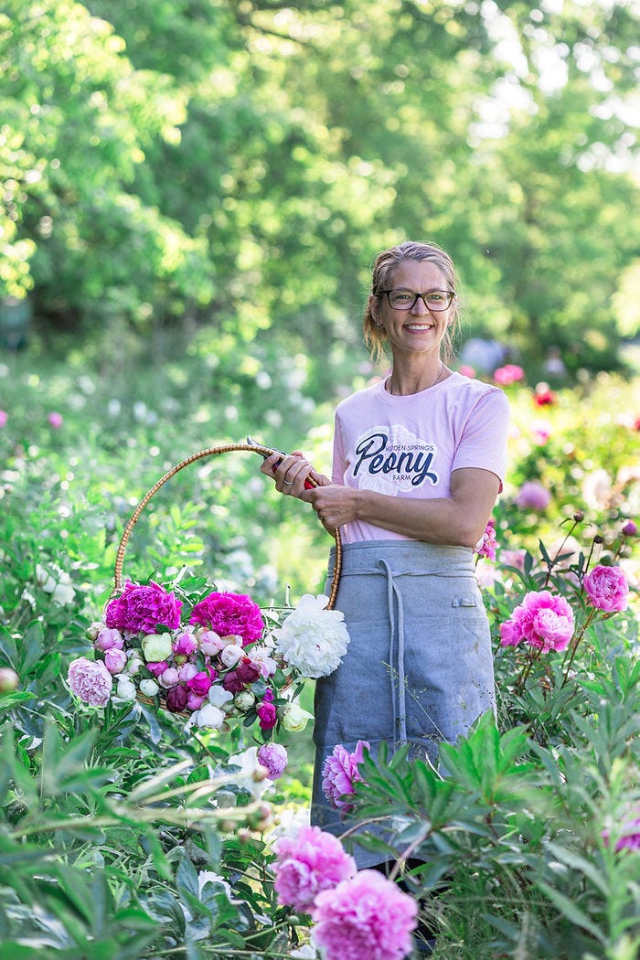 Laura Kubes joyfully harvests vibrant peonies from Hidden Springs Peony Farm, showcasing a basket brimming with colorful blooms.