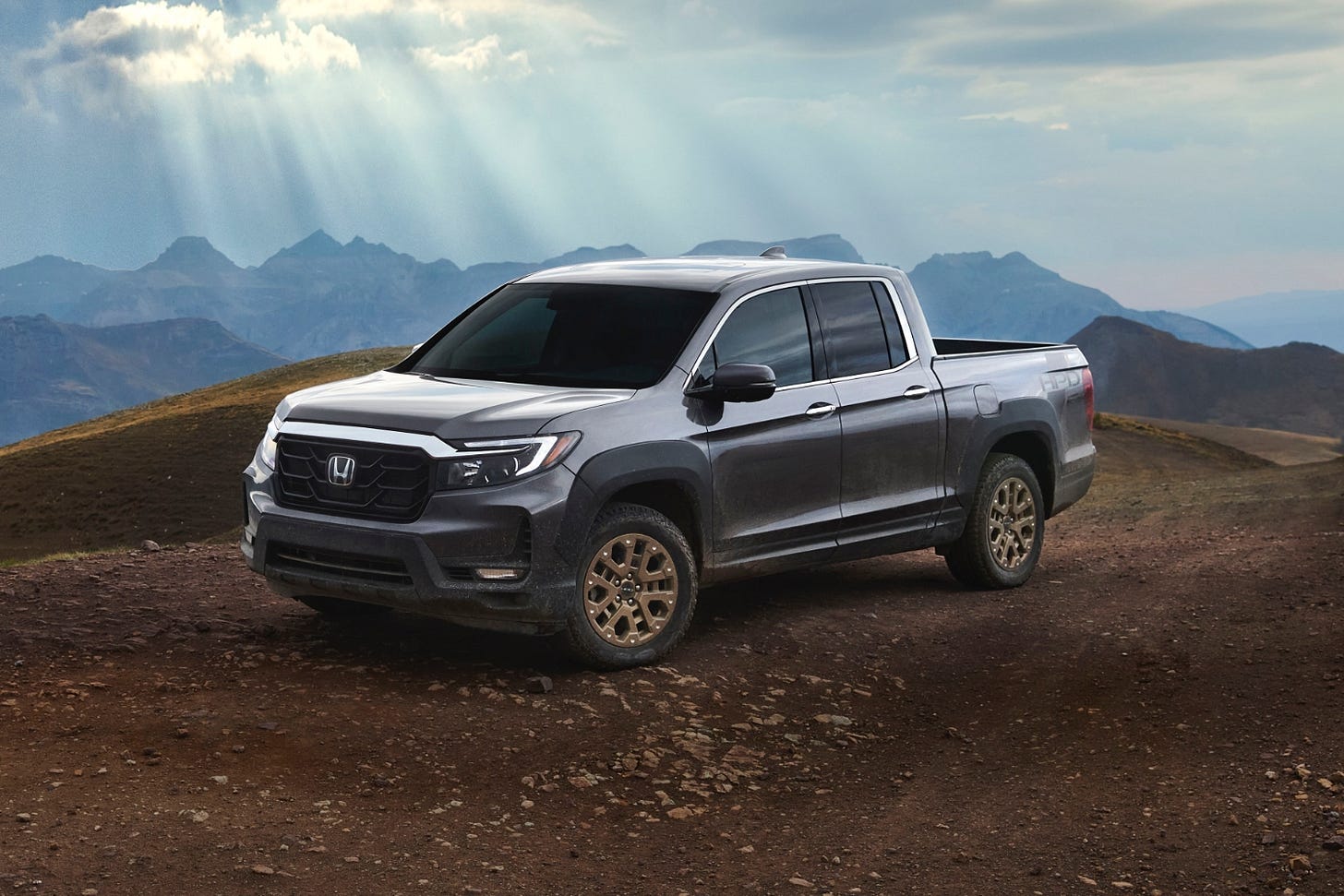 A gray 2023 Honda Ridgeline is parked on dirt in the mountains.