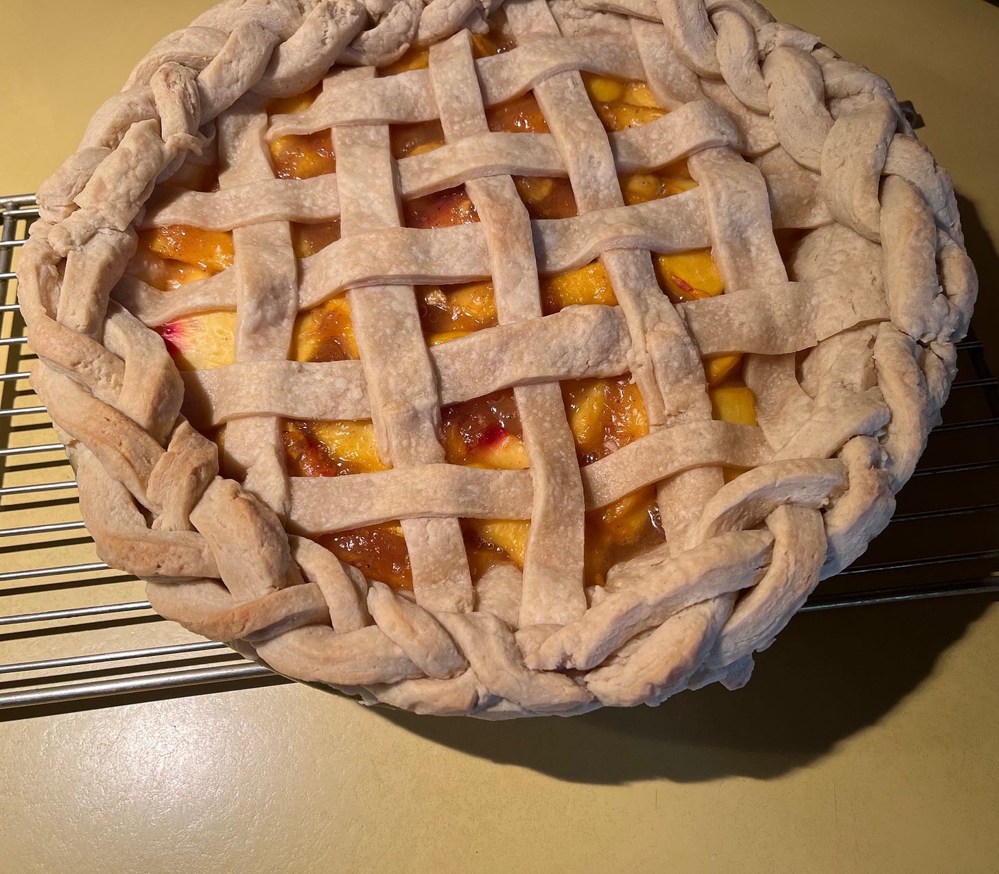 Photo of a peach pie on a rack on a harvest gold colored countertop.