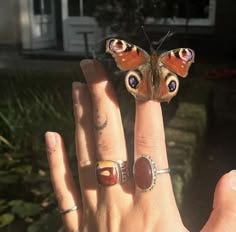 This may contain: a woman's hand with two rings and a butterfly on the middle finger, in front of a house