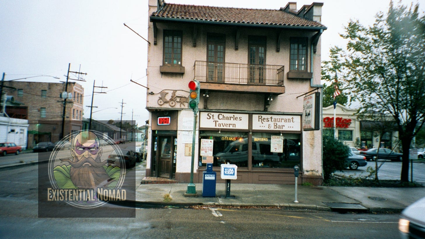  This is a photograph of a two-story corner building with a tiled roof. The building's sign identifies it as "St. Charles Tavern Restaurant & Bar." The street in front is wet, suggesting recent rain. There is a small balcony on the second floor, and a traffic light is visible on the corner. Cars are parked along the street, and in the background, other buildings and power lines can be seen.