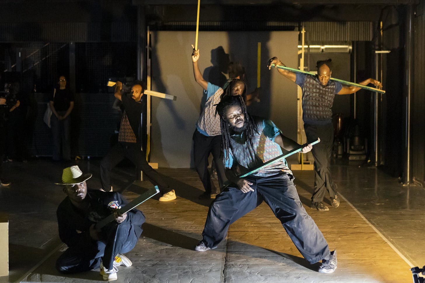 5 Tänzer*innen stehen in verschiedenen Positionen mit Holzstangen. 