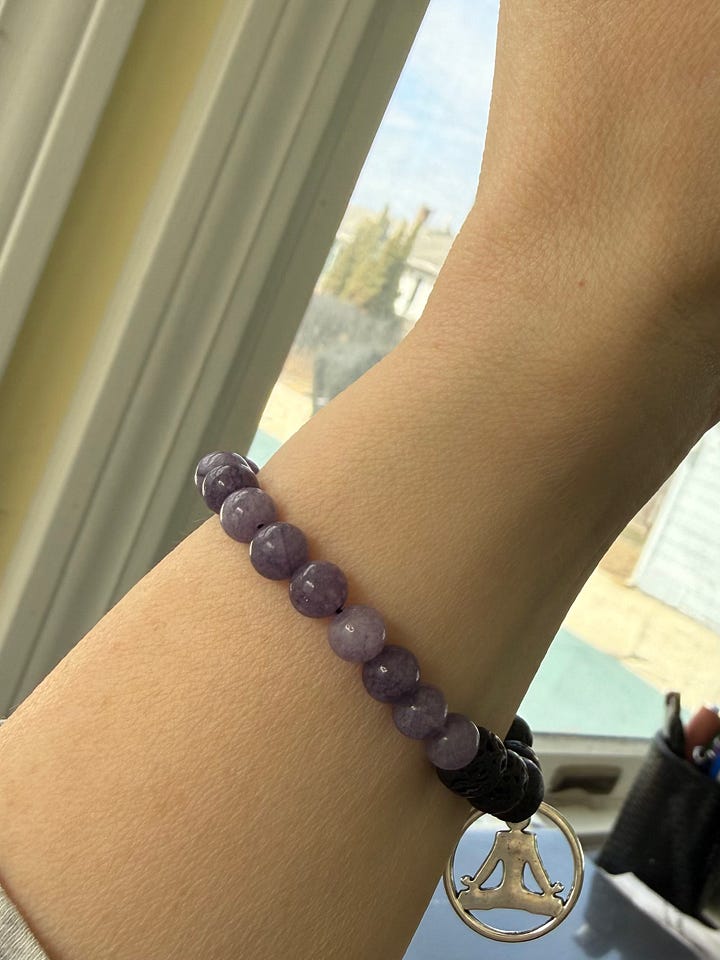 Two bracelets with lavender colored stones and lava rock. One has a shiny bead and the other a yoga charm.