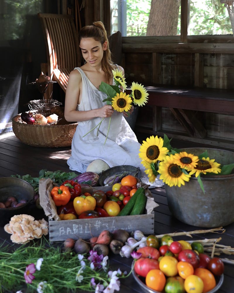 photo of a person sitting on the floor holding sunflowers and looking at crates and bowls full of colorful vegetables and fruits. photo of a person sitting on the floor holding sunflowers and looking at crates and bowls full of colorful vegetables and fruits.