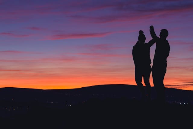 Silhouette of a couple standing together at sunset, one person reaching upward into a colorful sky, symbolizing growth, connection, and shared purpose. Silhouette of a couple standing together at sunset, one person reaching upward into a colorful sky, symbolizing growth, connection, and shared purpose.