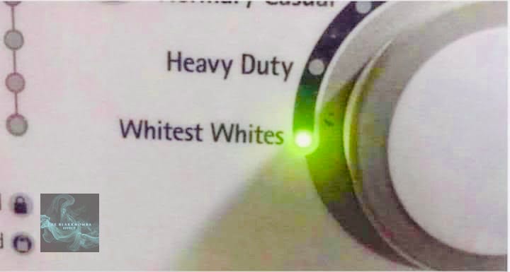 Close-up of a washing machine control dial set to “Whitest Whites,” with a green indicator light illuminated—used as a metaphor for systems that promise purity, protection, or superiority while masking mechanical violence and false safety.