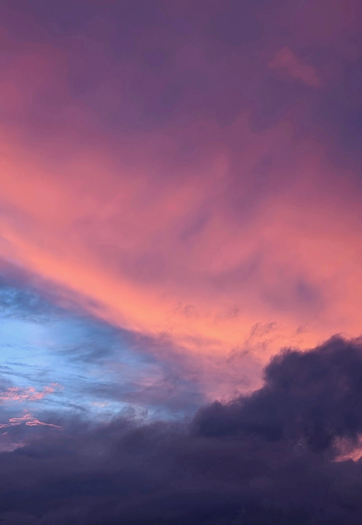 Fiery, pink clouds sweep the sky, in contrast to dark, looming clouds in the foreground, and hopeful pocket of blue to the left.
