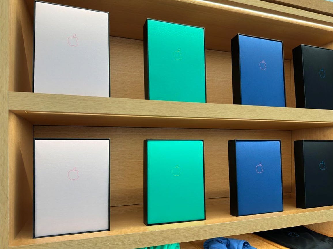 T-shirts displayed in the Avenues at Apple Infinite Loop. The shirts are pink, teal, blue, and black. Each shirt has an outlined Apple logo. T-shirts displayed in the Avenues at Apple Infinite Loop. The shirts are pink, teal, blue, and black. Each shirt has an outlined Apple logo.