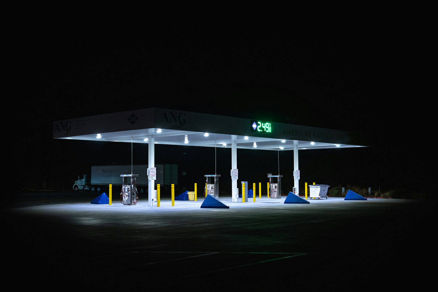 An empty, brightly lit truck stop at night with multiple fuel pumps under a white canopy, surrounded by darkness, with no people or vehicles visible.