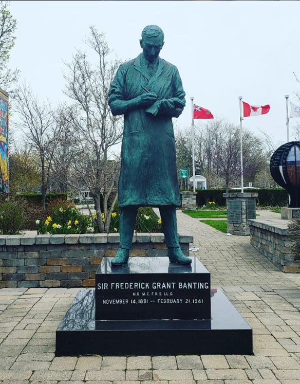 Statue of Dr. Frederick Banting in front of stone walls and two Canadian flags.