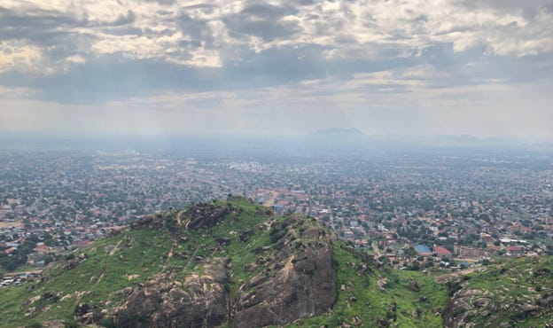 A person standing on a mountain looking at a city

Description automatically generated