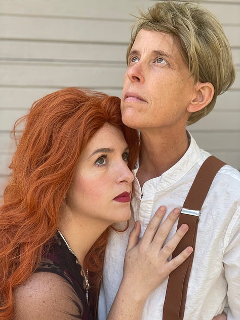 Megan Falley wears a curly red wig and maroon gown, Andrea Gibson wears a short blond wig, linen shirt and suspenders. They become Jack and Rose from Titanic, for a moment.