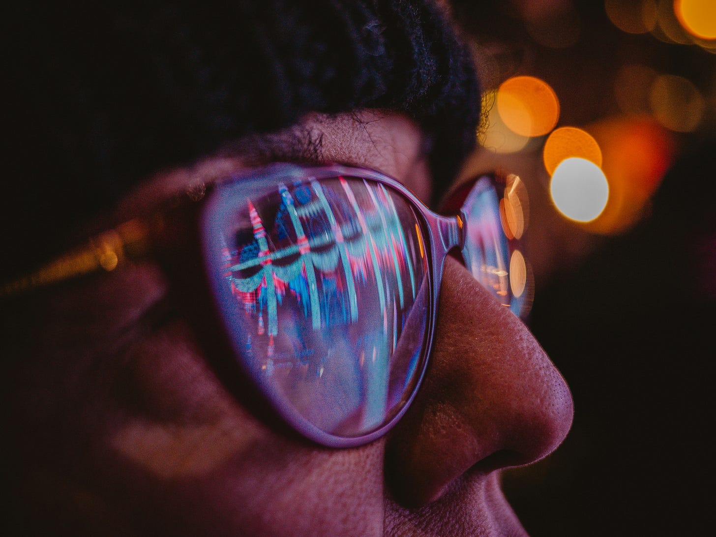 Close up of a person wearing glasses with colorful digital reflections in the lenses, symbolizing artificial intelligence, human computer interaction, and the future of technology.