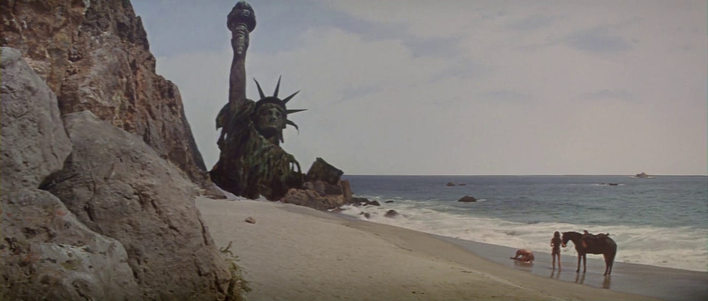 A still from the ending of the 1968 movie Planet of the Apes. The upper half of a partially destroyed Statue of Liberty sticks out from the beach as George Taylor (played by Charlton Heston) mourns and Nova (played by Linda Harrison) stands with their horse behind him, as the waves of the water crash down on the sand.