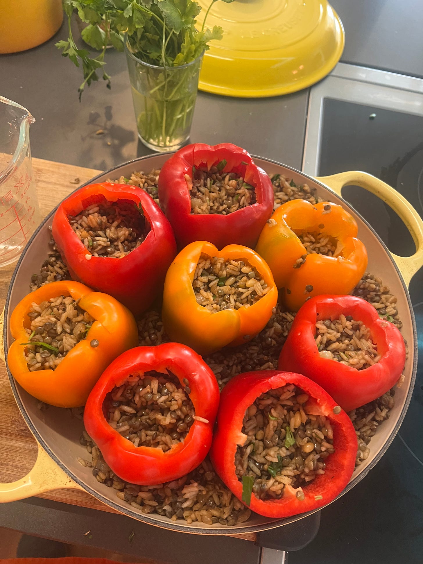 A yellow braiser with eight stuffed peppers in it.