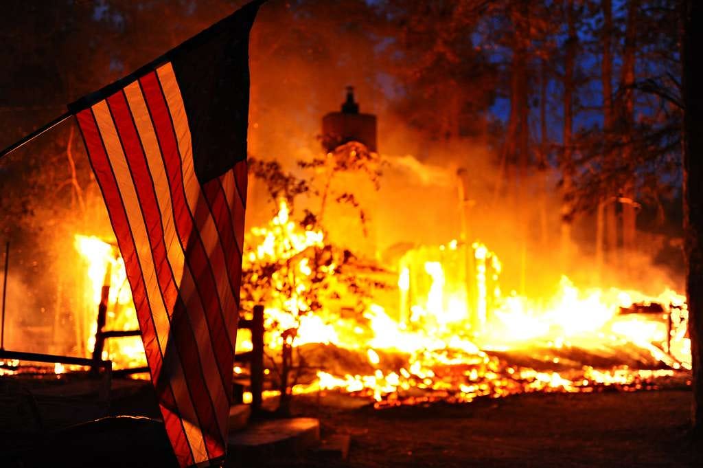 A U.S. flag hangs in front of a burning structure in — NARA and DVIDS Public Domain Archives A U.S. flag hangs in front of a burning structure in — NARA and DVIDS Public Domain Archives