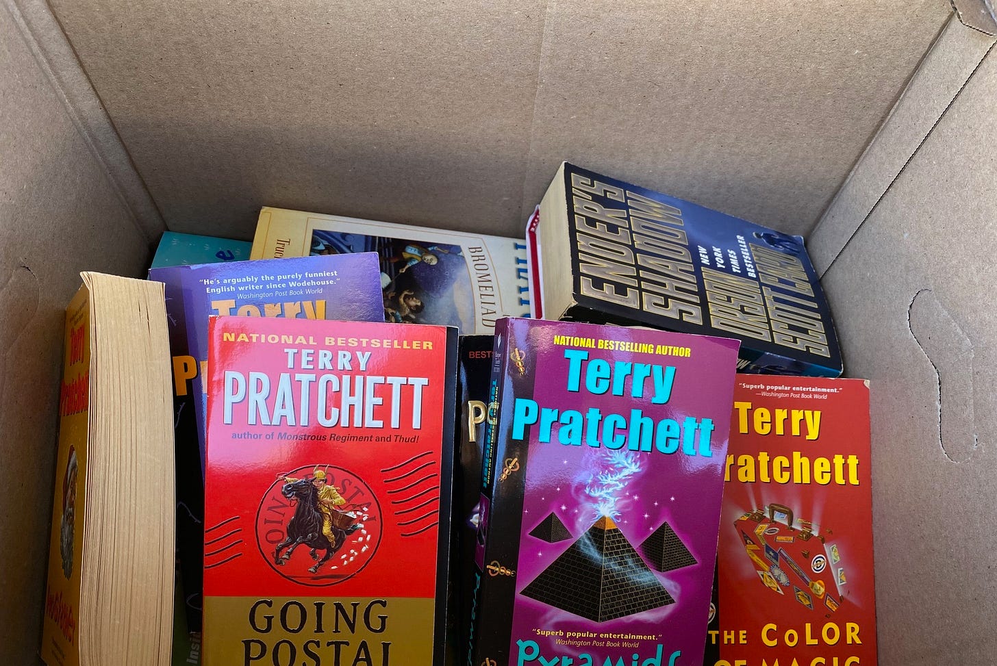 Pile of paperback books by author Terry Pratchett in a brown cardboard box.