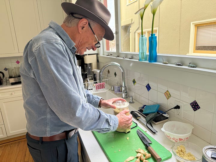 1. Hand in splint holding knife over ginger on a cutting board. 2. Man using a food process or to grate gi nger.
