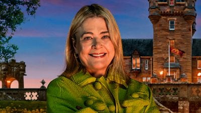 A woman in a green top smiles to camera, standing outside a castle by night A woman in a green top smiles to camera, standing outside a castle by night