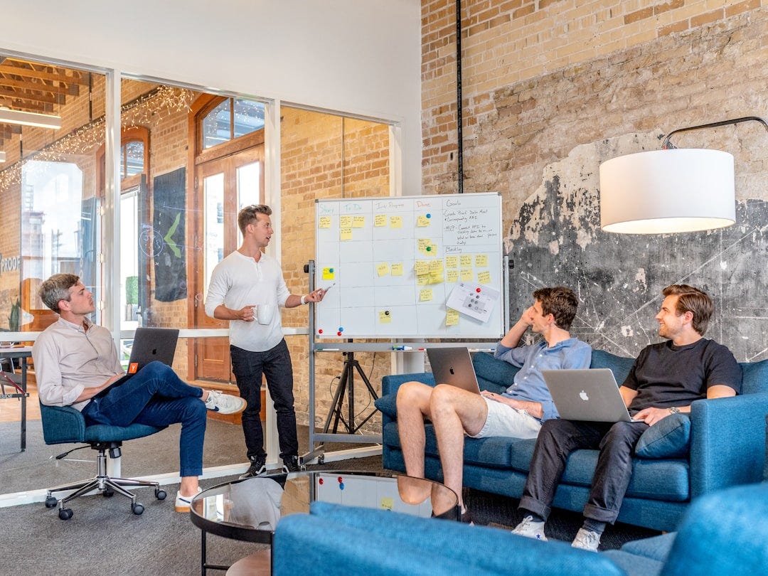 three men sitting while using laptops and watching man beside whiteboard three men sitting while using laptops and watching man beside whiteboard