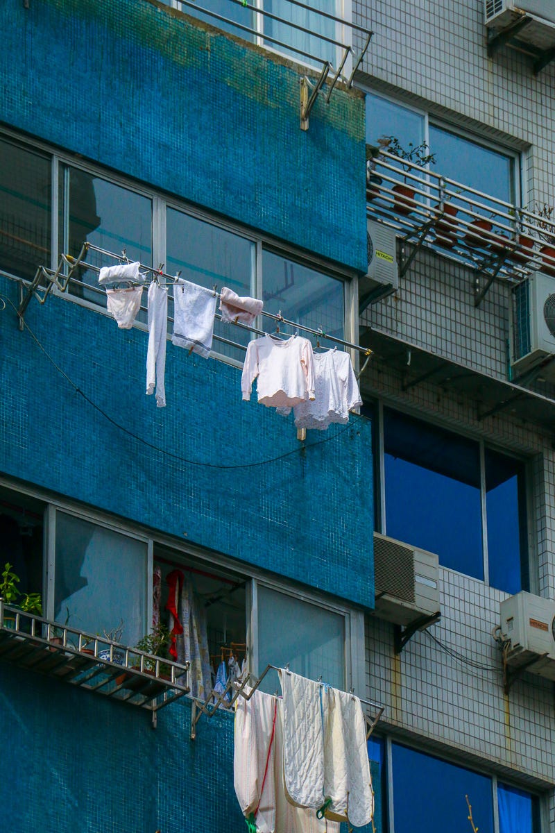White shirts and towels hang crisply against a vibrant blue tile facade. A minimalist but striking contrast of color and form in urban laundry life.