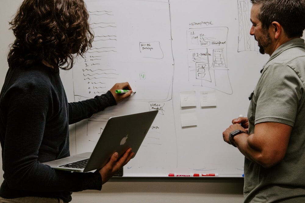 Colleagues writing on whiteboard (Credit: Kaleidico / Unsplash)
