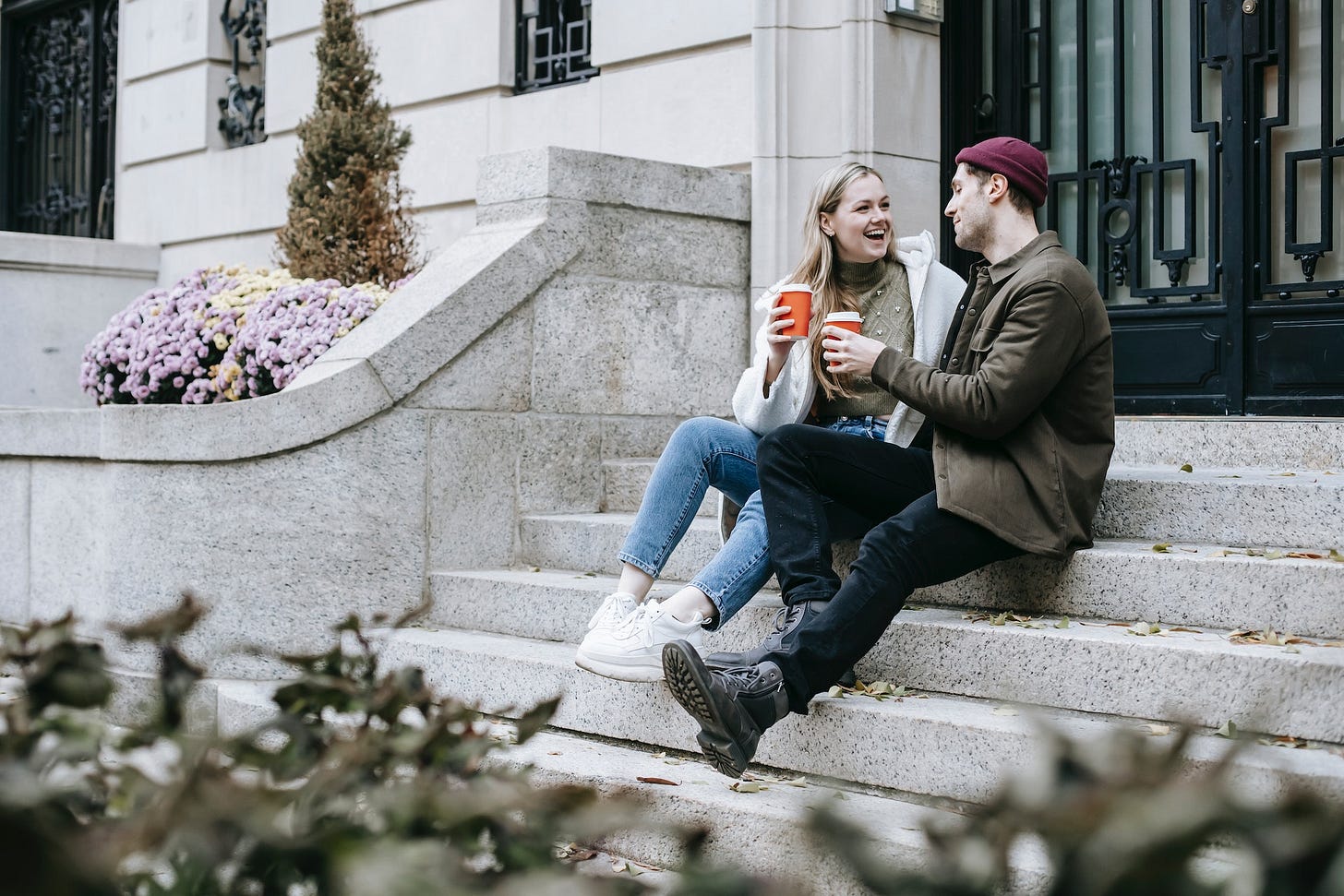 Cheerful friends sitting on steps with paper cups with hot coffee