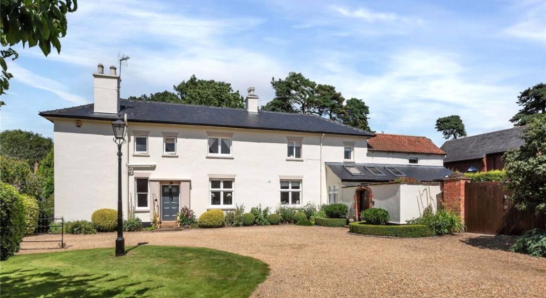 A large white house with a grey door and roof, with a gravel path in front of it and a blue sky above it