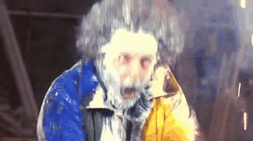 a man with a beard and frozen hair is wearing a blue and yellow jacket and looking at the camera . a man with a beard and frozen hair is wearing a blue and yellow jacket and looking at the camera .