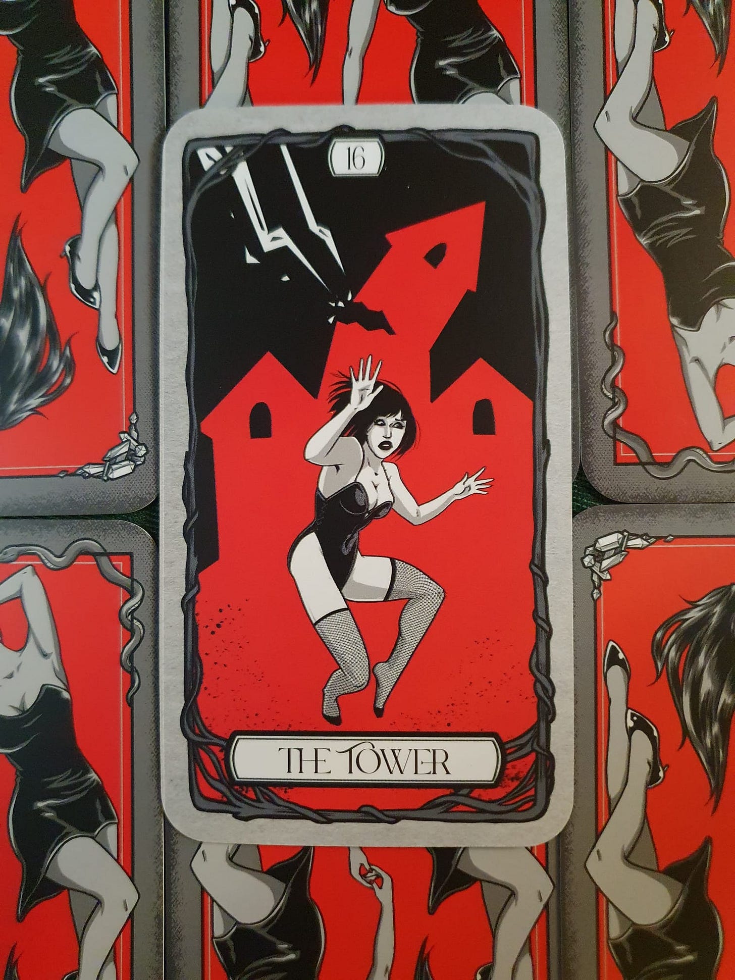 A gothic tarot card depicting The Tower, numbered 16. A woman in a black corset and fishnet stockings falls from a crumbling red tower struck by lightning. The illustration uses a dramatic red, black and grey colour palette, with decorative thorn borders. A gothic tarot card depicting The Tower, numbered 16. A woman in a black corset and fishnet stockings falls from a crumbling red tower struck by lightning. The illustration uses a dramatic red, black and grey colour palette, with decorative thorn borders.