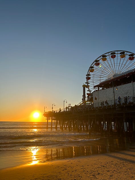 the pier sign, the pacific park sign, the end of route 66 sign, and the sun setting and rising over the pier