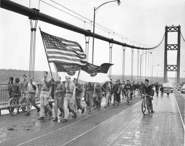 This may contain: black and white photograph of people walking on bridge with american flag