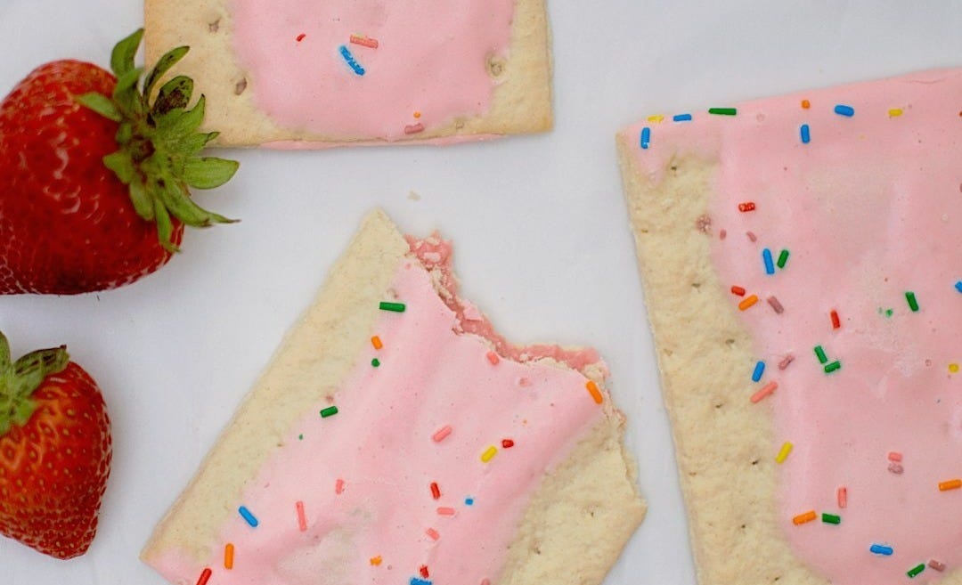 Pop-Tarts, des pâtisseries rectangulaires fourrées, glaçage rose et vermicelles colorés, posées sur fond blanc à côté de fraises. Pop-Tarts, des pâtisseries rectangulaires fourrées, glaçage rose et vermicelles colorés, posées sur fond blanc à côté de fraises.