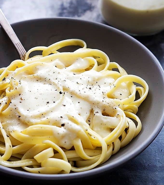 fettucine noodles with Greek yogurt alfredo sauce on top with a fork in a bowl with a jar with more sauce on the side. fettucine noodles with Greek yogurt alfredo sauce on top with a fork in a bowl with a jar with more sauce on the side.
