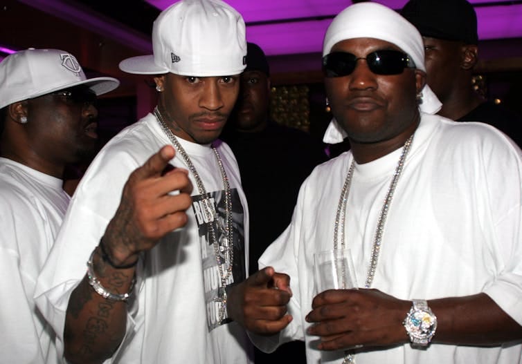 Three men wearing white hats, white T-shirts and diamond jewelry stand together