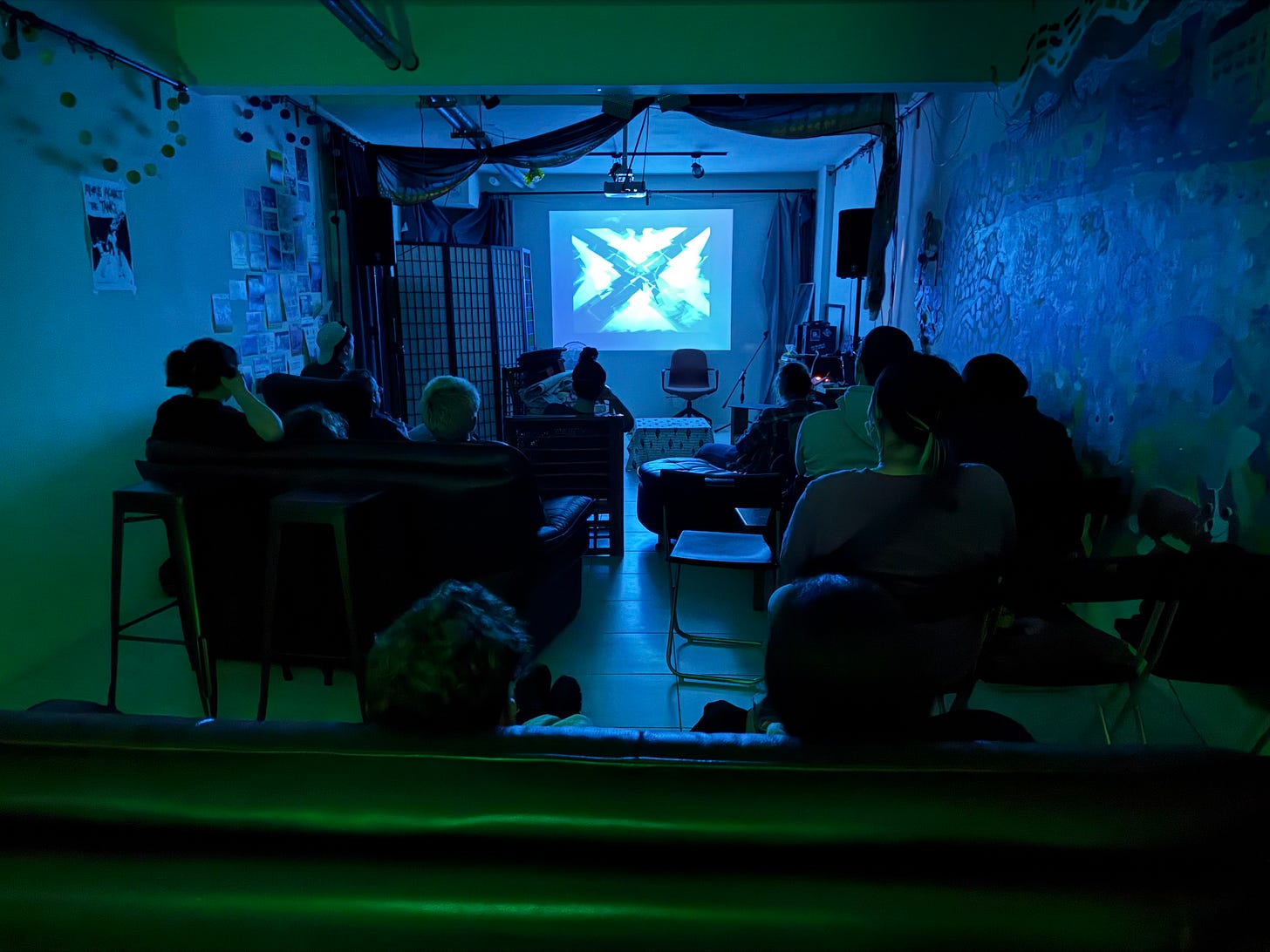 Horizontal photo of a darkened room with movie watchers heads peeking above sofas and chairs, staring at a film screen on Pen Club movie night.