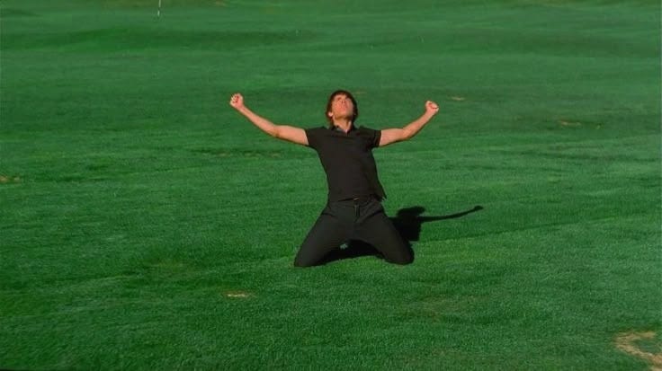 This may contain: a man jumping in the air with his arms wide open on a green grass covered field