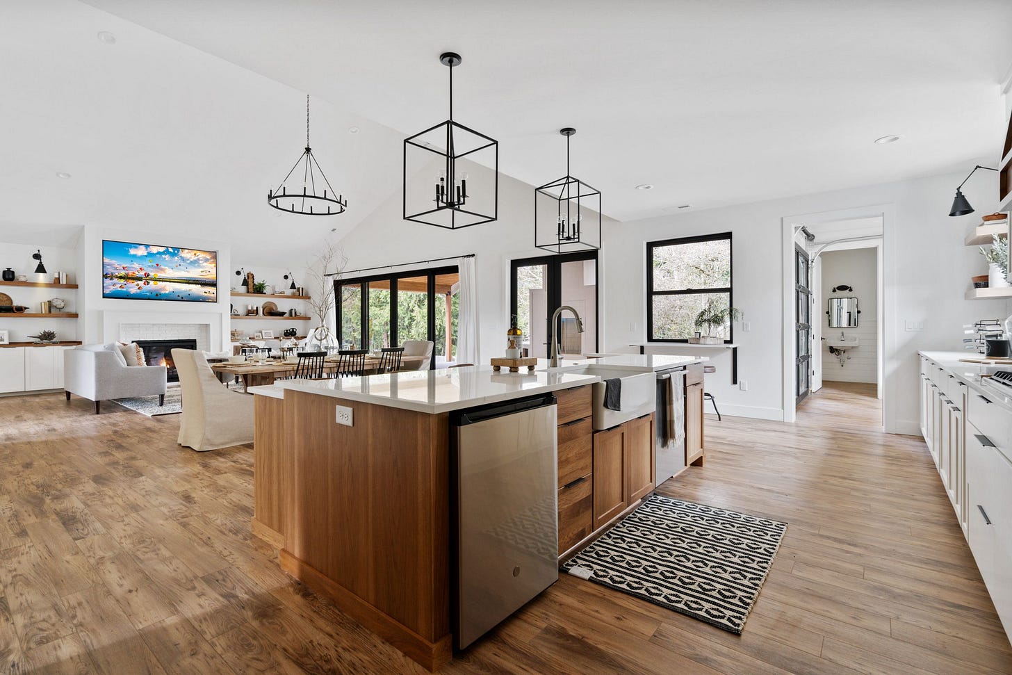 Spacious open floor plan with white walls and black fixtures shows an accessible kitchen, living room and the corner of a bathroom. 