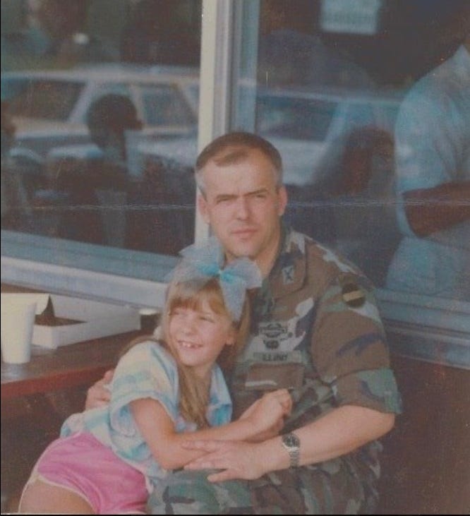 A photo of a young girl hugging her father who is wearing Army fatigues. The phot is from 1986. The girl wears a large hair bow. A photo of a young girl hugging her father who is wearing Army fatigues. The phot is from 1986. The girl wears a large hair bow.