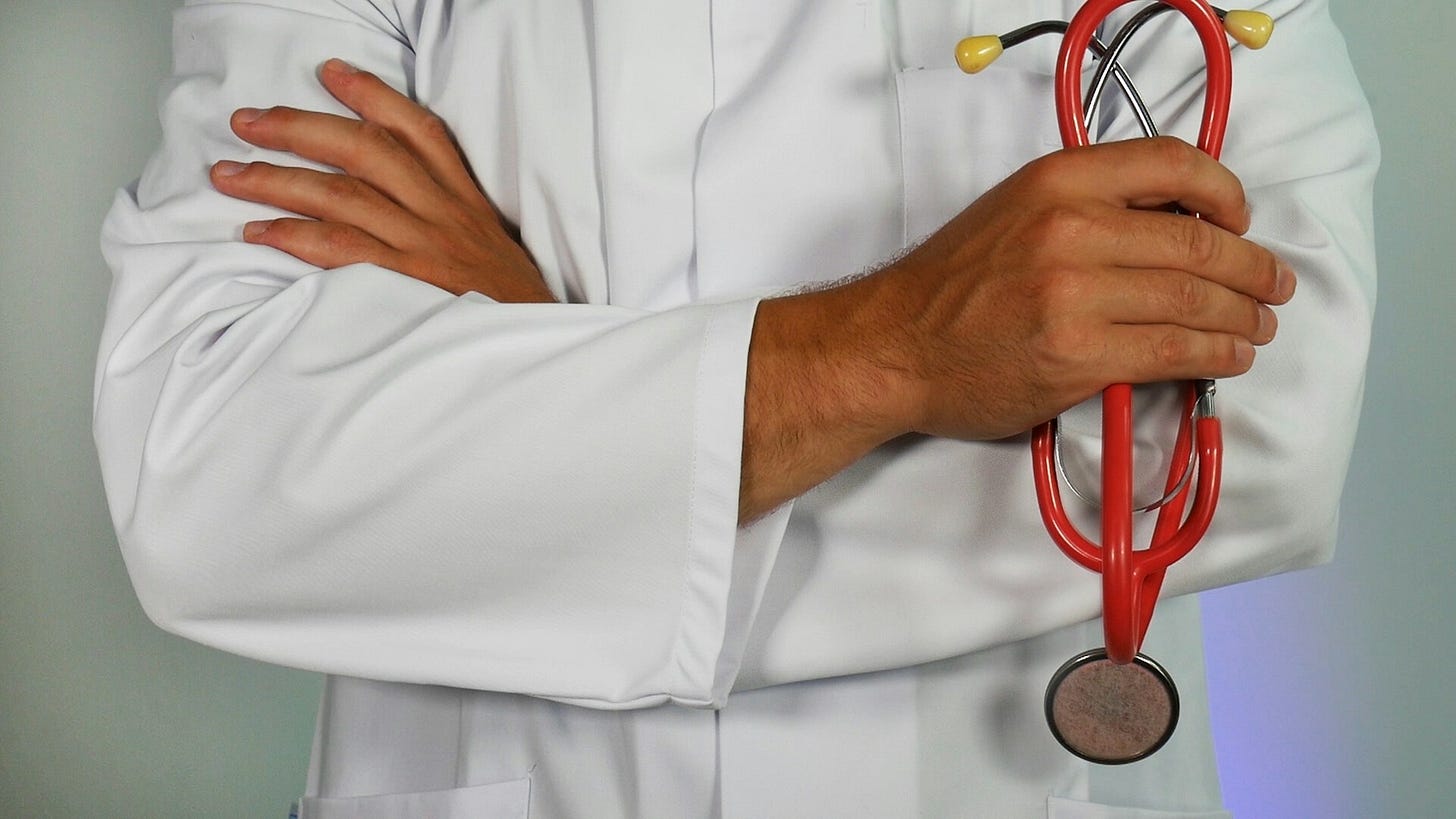 Doctor in a white coat with arms crossed, holding a red stethoscope.
