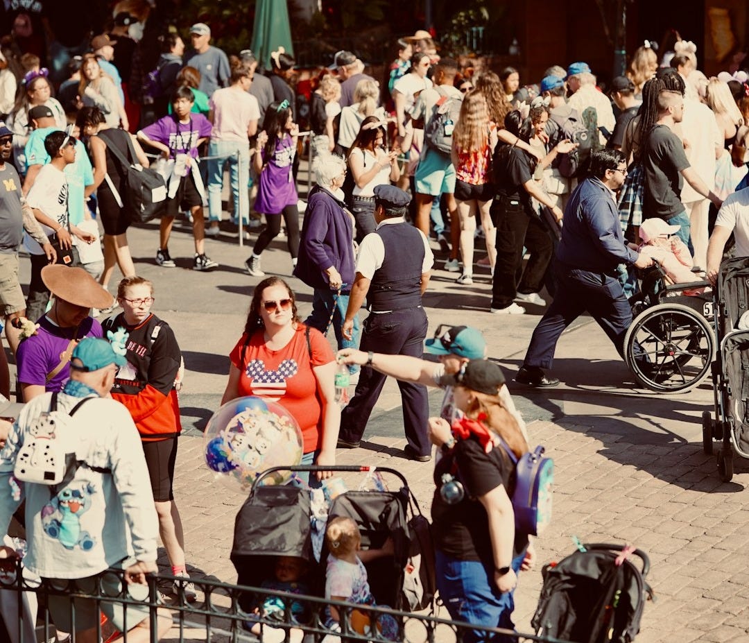 a crowd of people walking down a street next to a fence