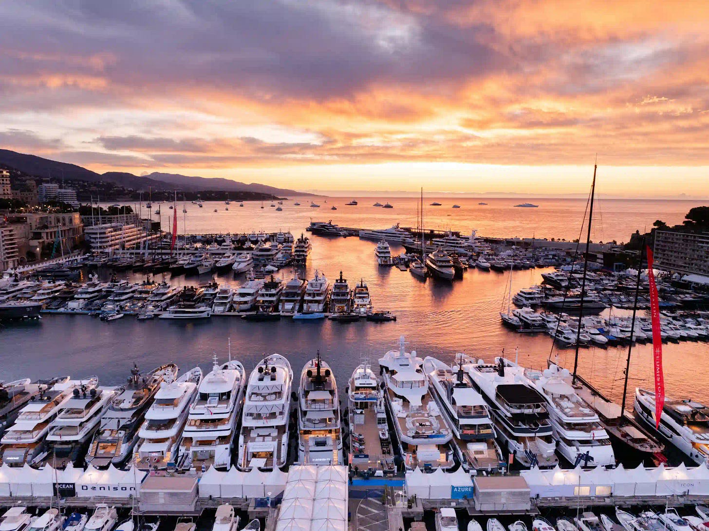 Majestic sunset view over Monacos harbor filled with superyachts, casting golden reflections across the sea.
