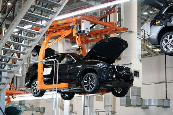 A shiny black car with its hood open is sitting on a hoist in a manufacturing plant. A shiny black car with its hood open is sitting on a hoist in a manufacturing plant.